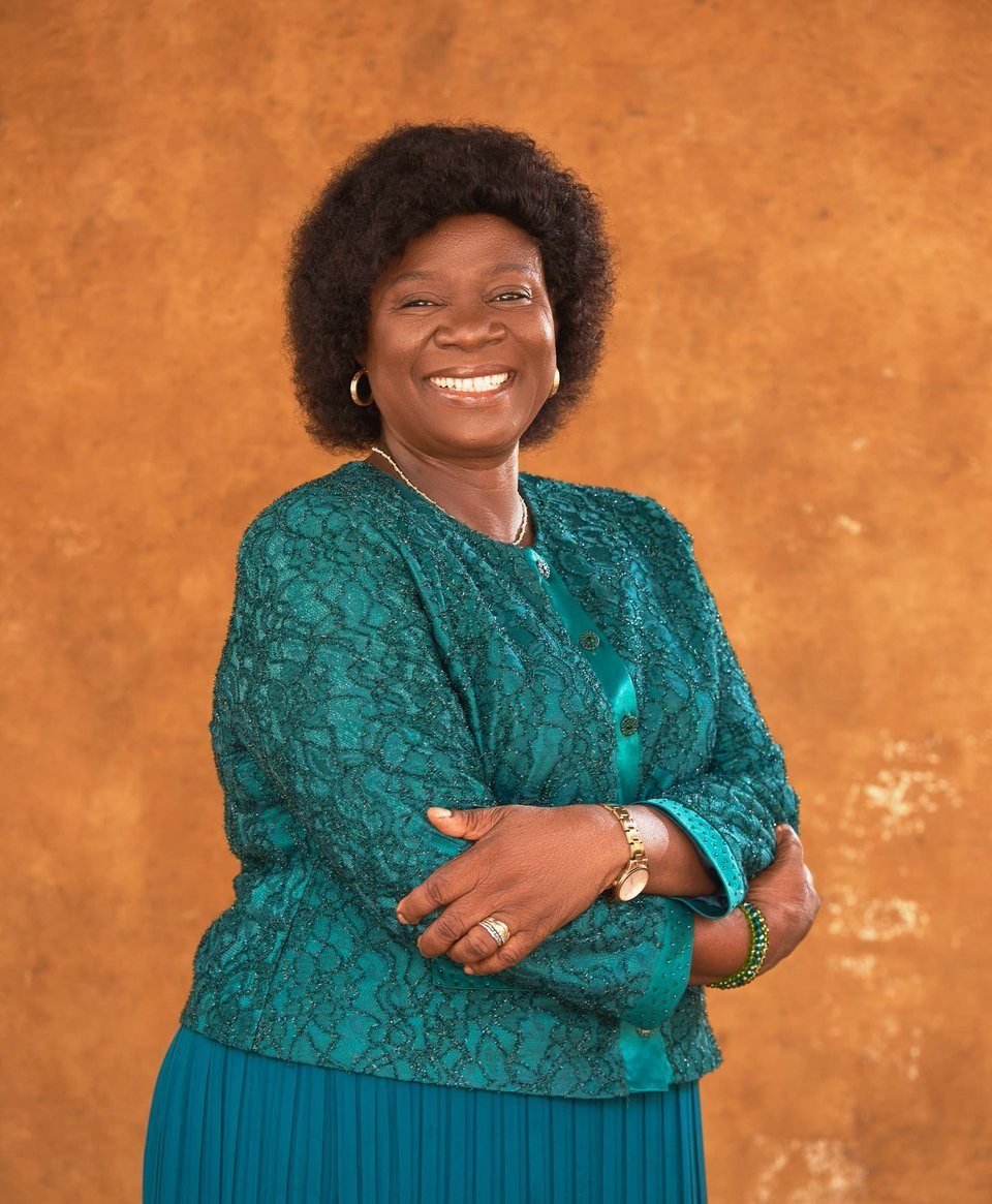 Professor Adejumo in a teal outfit, arms folded, smiling